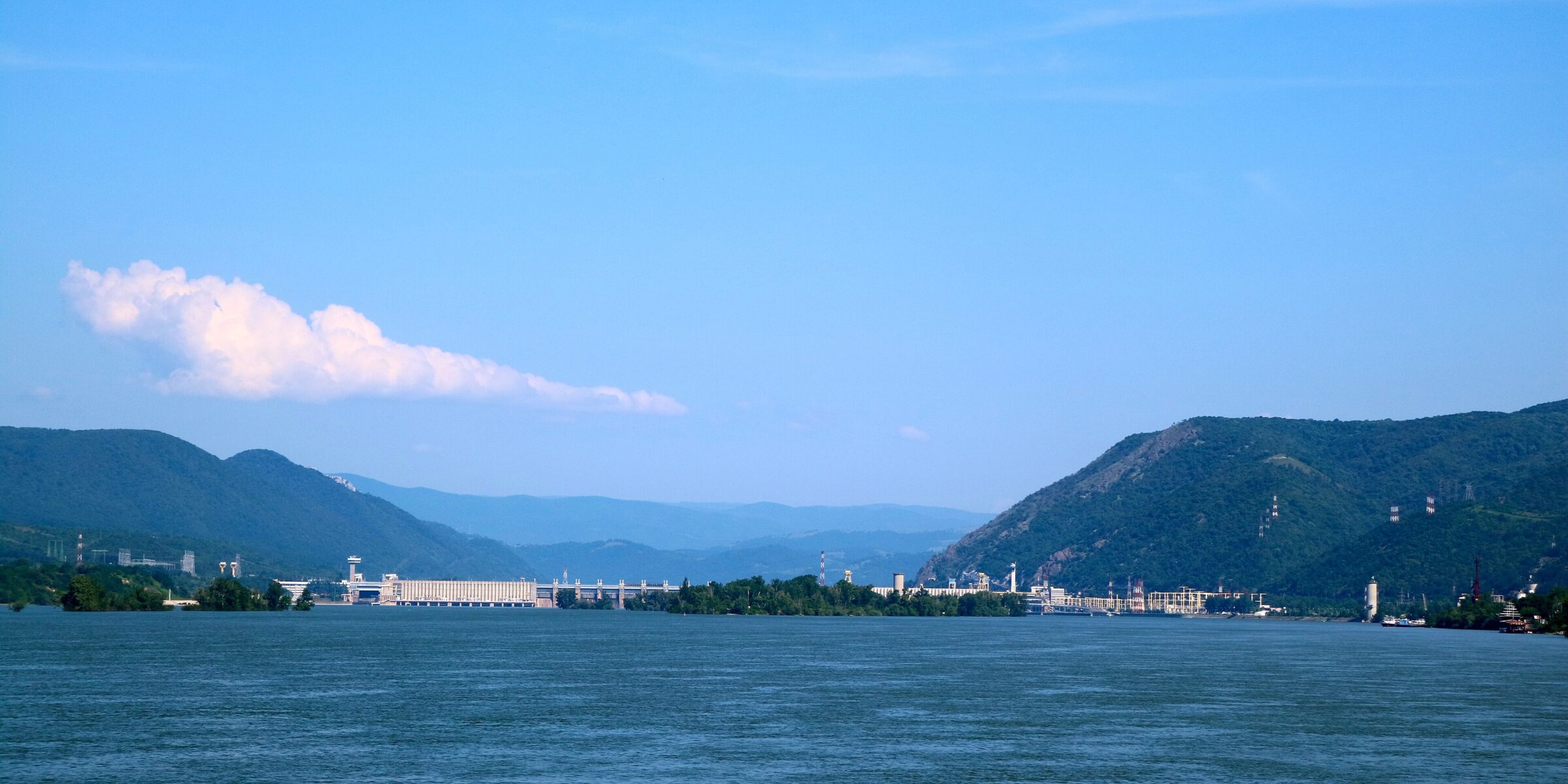 The Iron Gate I dam and power stations across the Danube between wooded hills, seen from the river